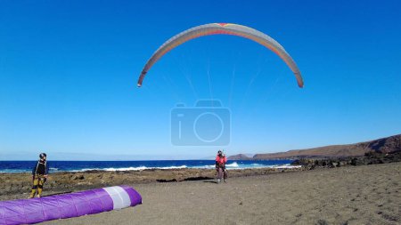 Photo for Spain, Lanzarote, Famara beach - The paraglider is the simplest and lightest means of free flight in existence - man wait for the wind in an ocean beach - Royalty Free Image