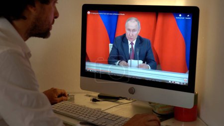 Téléchargez les photos : Europe, Milan 2023 - Regarder la télévision Nouvelles dans un ordinateur portable sur la guerre entre la Russie et l'Ukraine - Poutine parle à la nation - en image libre de droit
