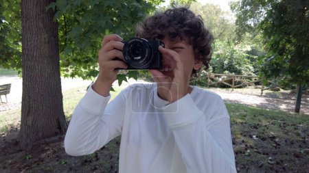 Foto de Niño de 9 años tomando fotos con la cámara en un parque durante las vacaciones - viajar y aprender a tomar fotos en la infancia - Imagen libre de derechos