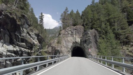 Photo for Mountain road entering a stone tunnel in the rock view from the car - holidays and travel in nature italian Swiss Alps - Royalty Free Image