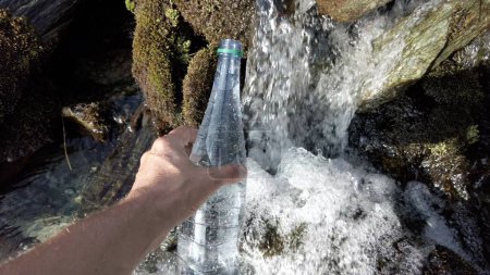 Foto de Llenando la botella de agua en un arroyo de montaña - deshielo de los glaciares y agua potable en el río - no hay uso de plástico y una opción ecológica para el medio ambiente - Save the Planet - Imagen libre de derechos