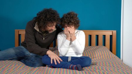 9-jähriger Junge weint im Schlafzimmer, während sein Vater versucht, ihn zu beruhigen 