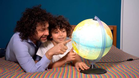 Téléchargez les photos : Père et fils regardent le monde et rêvent où voyager dans le futur, mode de vie pendant l'enfance et désir de voyager et de découvrir le monde - concept de changement climatique et de réchauffement climatique - en image libre de droit