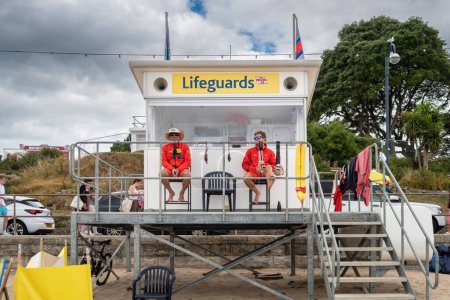 Foto de 2 socorristas sentados fuera de la estación de socorristas en la playa Swanage en Dorset observando la playa y el mar para mantener a las personas seguras - Imagen libre de derechos