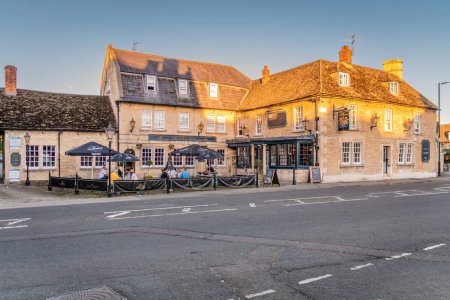 Photo for The Kings Arms hotel in Melksham Wiltshire with its sandy stone brickwork glowing orange in the setting sun and customers socializing outside - Royalty Free Image