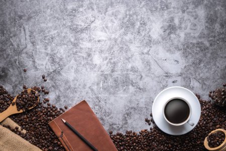 Foto de El café está en una taza blanca con un cuaderno de cuero y lápiz colocado en el piso viejo y rodeado de muchos granos de café, con espacio para copiar. - Imagen libre de derechos