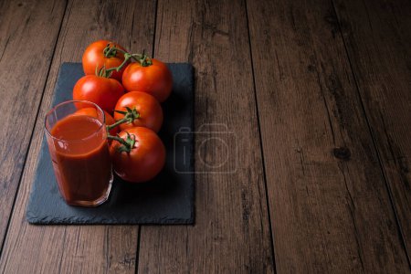 Foto de Jugo de tomate en un vaso y un tomate fresco junto a él en una mesa de madera. - Imagen libre de derechos