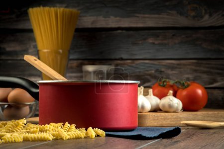 Foto de Varios ingredientes para hacer espaguetis como espaguetis en un vaso, tomates, champiñones, orégano, varios condimentos y una olla para cocinar colocada en una mesa de madera. - Imagen libre de derechos