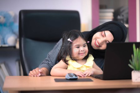 Foto de Una hermosa madre musulmana está jugando con una linda hija y aprendiendo cosas a través de la computadora en su casa. - Imagen libre de derechos