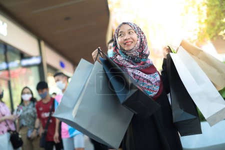 Foto de Una mujer musulmana asiática está llevando una bolsa de bienes que ha estado comprando y comprando muchos productos con caras felices y felices.. - Imagen libre de derechos