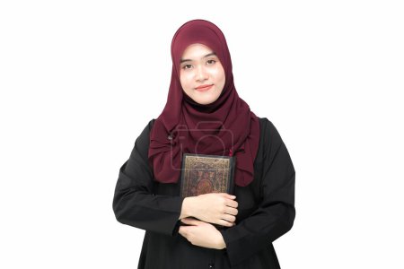 Photo for Portrait Asian Muslim woman standing and reading the Quran and appreciates and faith The Holy Al Quran with written Arabic calligraphy meaning of Al Quran, Arabic word translation : The Holy Al Quran. - Royalty Free Image