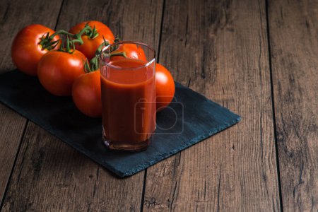 Foto de Jugo de tomate en un vaso y un tomate fresco junto a él en una mesa de madera - Imagen libre de derechos