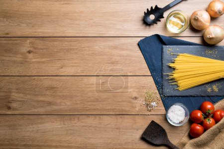 Foto de Varios ingredientes para hacer espaguetis como espaguetis, tomates, orégano y varios condimentos colocados en una mesa de madera, con espacio para copiar, vista superior. - Imagen libre de derechos