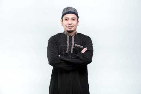 Foto de La imagen de un musulmán asiático de pie con los brazos cruzados con una cara sonriente, sobre fondo blanco. - Imagen libre de derechos