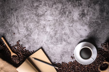 Foto de El café está en una taza blanca con un cuaderno de cuero y lápiz colocado en el piso viejo y rodeado de muchos granos de café, con espacio para copiar. - Imagen libre de derechos
