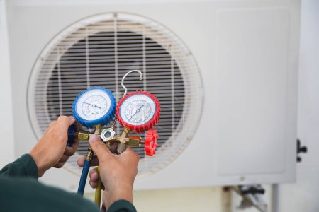 Aire acondicionado, técnico de servicio de climatización que utiliza medidores para comprobar el refrigerante y añadir refrigerante.
