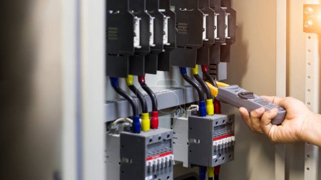 Téléchargez les photos : Testeur de travail ingénieur électricien mesurant la tension et le courant de la ligne électrique dans le contrôle de l'armoire électrique. - en image libre de droit