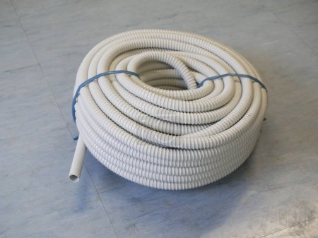 Téléchargez les photos : Rouleau de fil flexible ondulé gris PVC Conduit sur plancher bleu clair - en image libre de droit