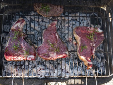 Photo for Four beef steaks grilled on the barbecue and seasoned with rosemar - Royalty Free Image