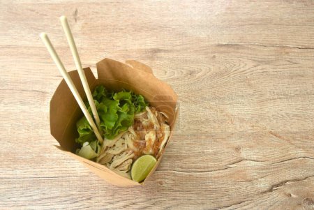 noodles packaged in hard brown paper box for take home with wooden chopsticks on table