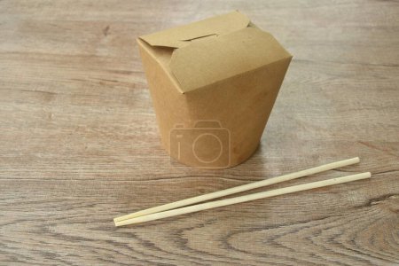 noodles packaged in hard brown paper box for take home with wooden chopsticks on table