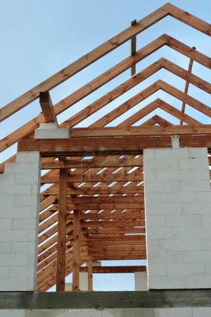Photo for A timber roof truss in a house under construction, walls made of autoclaved aerated concrete blocks, blue sky in the background - Royalty Free Image