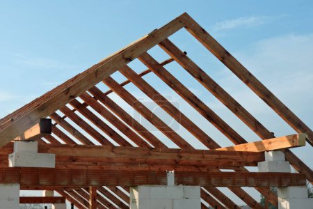 Foto de Una armadura de techo de madera en una casa en construcción, paredes hechas de bloques de hormigón aireado en autoclave, aberturas de ventanas ásperas, un dintel de ladrillo reforzado, cielo azul en el fondo - Imagen libre de derechos
