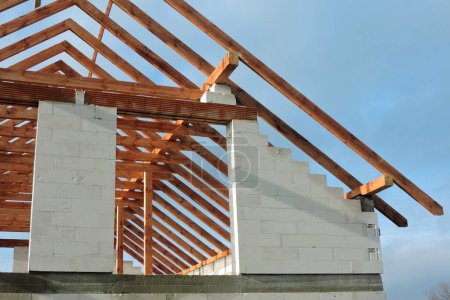 Foto de Una armadura de techo de madera en una casa en construcción, paredes hechas de bloques de hormigón aireado en autoclave, una abertura de ventana áspera, un dintel de ladrillo reforzado, cielo azul en el fondo - Imagen libre de derechos