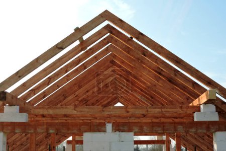 Foto de A timber roof truss in a house under construction, walls made of autoclaved aerated concrete blocks, rough window openings, reinforced brick lintels, blue sky in the background - Imagen libre de derechos