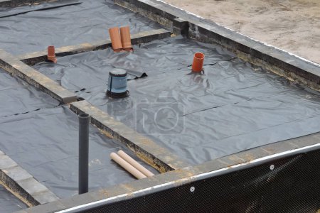 Foto de Membrana a prueba de humedad colocada bajo una base de losa, paredes de cimentación aisladas y una instalación de plomería y agua - Imagen libre de derechos