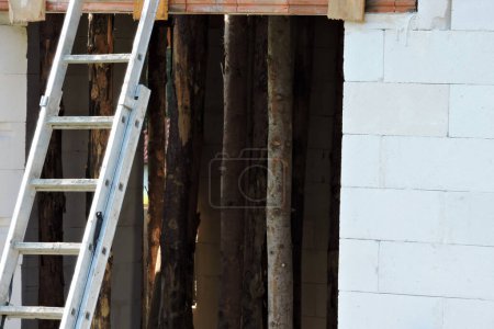 Foto de A ladder leaning against a wall, a rough window opening, reinforced brick lintels, walls made of autoclaved aerated concrete and wooden building props inside a house under construction - Imagen libre de derechos