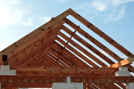 Foto de Una armadura de techo de madera en una casa en construcción, paredes hechas de bloques de hormigón aireado en autoclave, aberturas de ventanas ásperas, un dintel de ladrillo reforzado, un andamio, cielo azul en el fondo - Imagen libre de derechos
