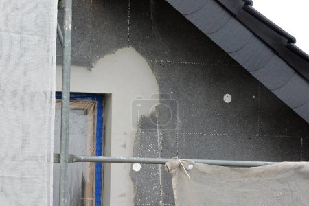 Photo for A wall of a house covered with EPS graphite polystyrene boards for thermal insulation, a window covered with a protective film, a scaffolding, anchors - Royalty Free Image