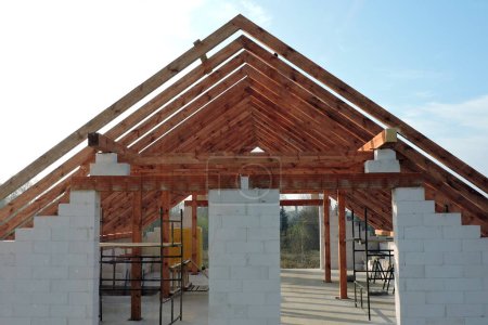 Une poutre de toit en bois à ossature "A" dans une maison en construction, des murs en blocs d'aac, une ouverture de fenêtre rugueuse, un linteau en brique renforcée, un échafaudage, un ciel bleu en arrière-plan