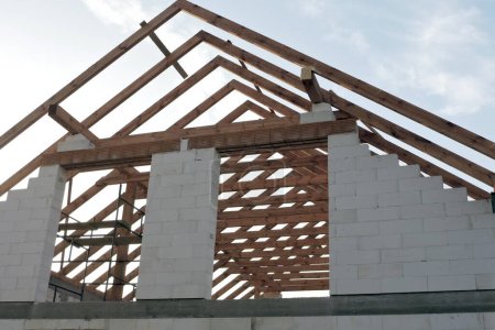 Une poutre de toit en bois à ossature "A" dans une maison en construction vue du bas, des murs en blocs d'aac, une ouverture de fenêtre rugueuse, un linteau en brique renforcée, un échafaudage