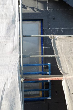 Photo for A wall of a house covered with EPS graphite polystyrene boards for thermal insulation, a window covered with a protective film, a scaffolding, a sunny day - Royalty Free Image