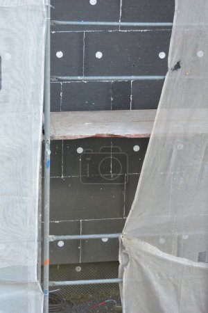 Photo for A wall of a house covered with EPS graphite polystyrene boards for thermal insulation, a scaffolding and building safety scaffolding net, anchors - Royalty Free Image