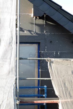 Photo for A wall of a house covered with EPS graphite polystyrene boards for thermal insulation, a window covered with a protective film, a scaffolding - Royalty Free Image