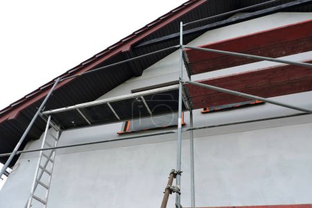 A scaffolding near a wall which is covered with prime before rendering exterior walls, windows and windowsills covered with a protective film, bottom view