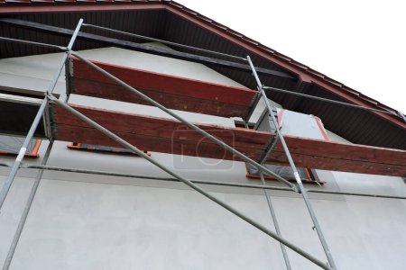 A scaffolding near a wall which is covered with prime before rendering exterior walls, windows and windowsills covered with a protective film, bottom view