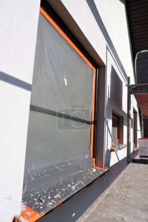 Windows and windowsills covered with a protective film, an exterior wall which is covered with prime and partially rendered