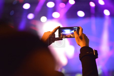 Foto de Manos de la chica que graba el escenario con un teléfono móvil durante un concierto - Imagen libre de derechos