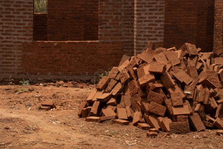 Foto de Una pila de ladrillos de barro quemados, un material de construcción común en África, frente a un edificio de construcción media. - Imagen libre de derechos