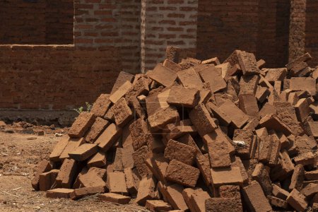 Foto de Una pila de ladrillos de barro quemados, un material de construcción común en África, frente a un edificio de construcción media. - Imagen libre de derechos