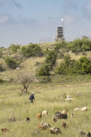 Photo for Jerusalem, Israel - May 6th, 2022: A herd of goats and sheep with their shepherd near an Iron Dome anti rocket battery, deployed in the Judea mountains, near Jerusalem, Israel. - Royalty Free Image