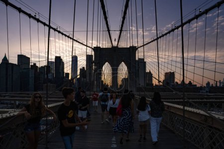 Foto de Nueva York, Estados Unidos - 23 de julio de 2023: Turistas en el puente de Brooklyn al atardecer, con la línea del cielo de Manhattan al fondo. - Imagen libre de derechos
