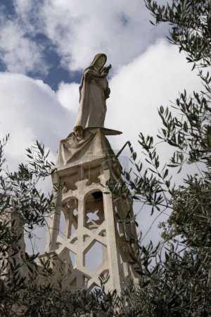 Photo for Abu Ghosh, Israel - March 7th, 2024: The statue of the madonna and child, on top of the church of Our Lady of the Ark of the Covenant in Abu Ghosh, Israel, viewed through olive branches. - Royalty Free Image
