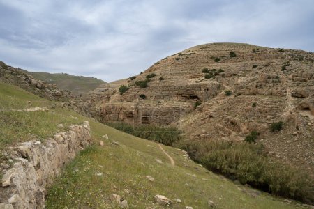 Uralte Steinmauern, Fußwege und Höhlen schmücken die Hügel der Wüste Judäa, die den Fluss Prat umgeben. Die Hügel sind nach dem Winter in Grün gehüllt.