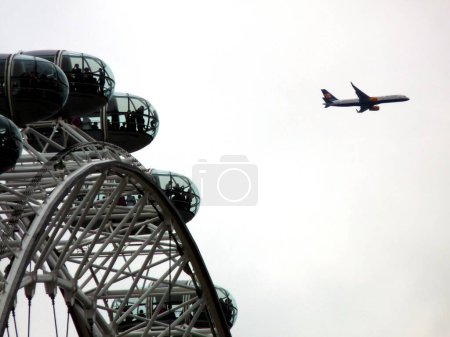 Teilansicht des London Eye mit einem vorbeifliegenden Flugzeug am Himmel, London, UK, viel Kopierraum Hochwertiges Foto