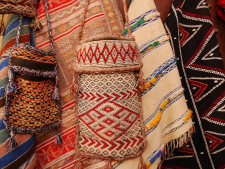 Auswahl an handgefertigten marokkanischen Stofftaschen und Decken in hellen traditionellen Mustern und lebendigen Farben, teilweise mit Quasten